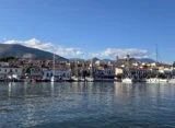 Panoramic view of Galaxidi’s historic harbour, with traditional waterfront houses, moored sailing boats, a red-domed church and mountains in the background.