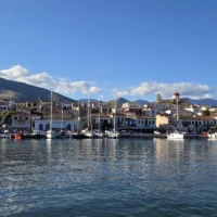 Panoramic view of Galaxidi’s historic harbour, with traditional waterfront houses, moored sailing boats, a red-domed church and mountains in the background.