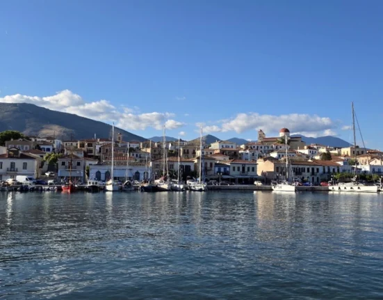 Panoramic view of Galaxidi’s historic harbour, with traditional waterfront houses, moored sailing boats, a red-domed church and mountains in the background.
