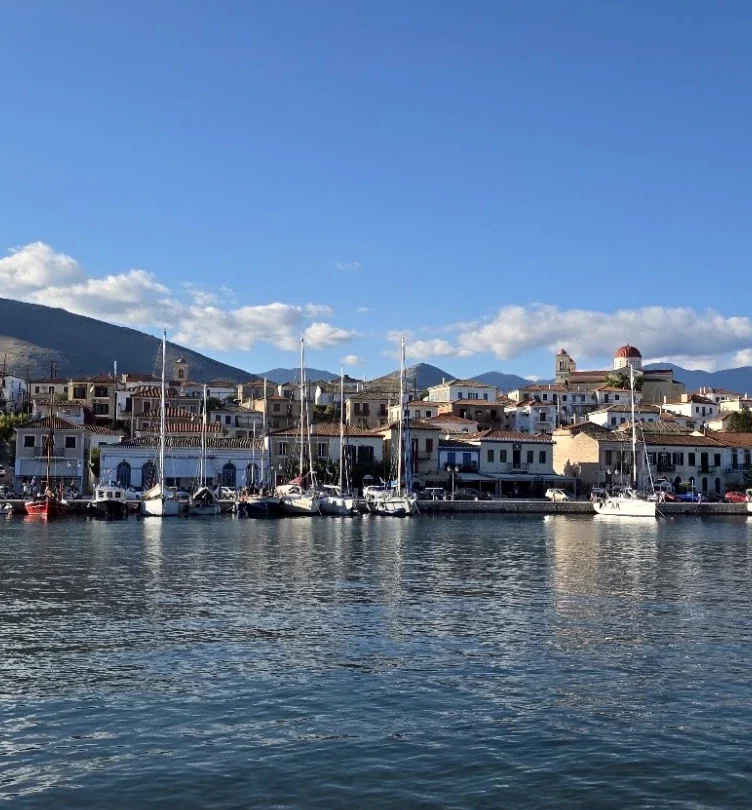 Panoramic view of Galaxidi’s historic harbour, with traditional waterfront houses, moored sailing boats, a red-domed church and mountains in the background.