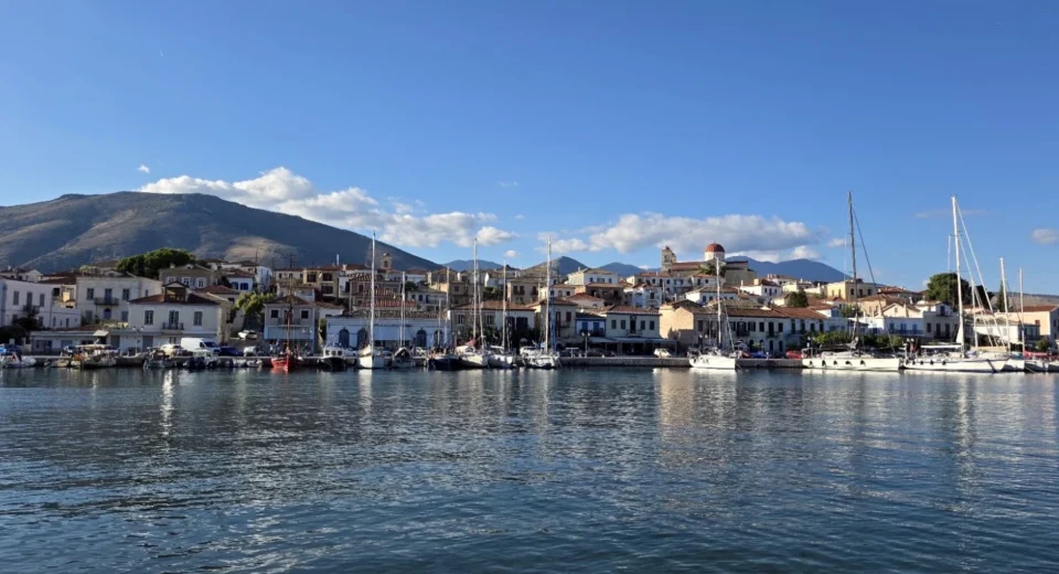 Panoramic view of Galaxidi’s historic harbour, with traditional waterfront houses, moored sailing boats, a red-domed church and mountains in the background.