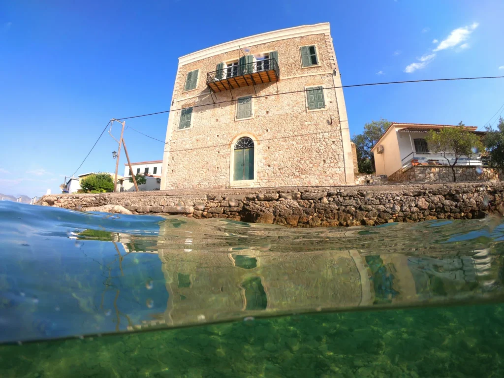 Bourzeiko, a historic stone captain's house on the Chirolakas waterfront in Galaxidi, with green shutters and an iron balcony