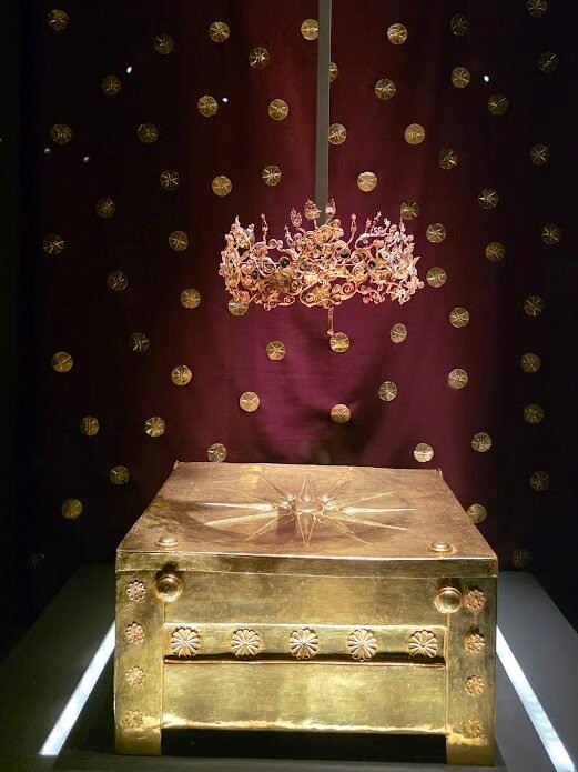 Gold Larnax and Gold Diadem of Meda, the young royal wife of Philip II, with the larnax once holding her remains and the diadem surviving the funeral pyre. Background shows golden star-embossed roundels from the antechamber of Philip’s tomb. Museum of the Royal Tombs of Aigai, Expats Athens, Expats Greece, Xpat.gr