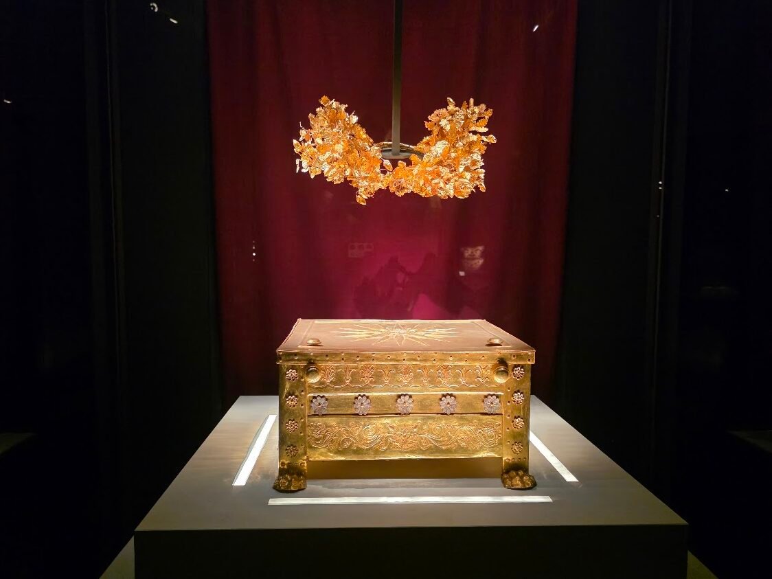Gold Larnax of King Philip II with the Gold Oak Wreath that crowned him on the funeral pyre. This 4th-century BCE ash chest, crafted from hammered 24-karat gold and weighing 7.82 kg, features the 16-rayed Vergina Sun, rosettes, palmettes, lotus buds, and lion-paw feet. The wreath, with 313 leaves and 68 acorns, partially melted in the pyre, is the heaviest surviving Greek gold wreath. Museum of the Royal Tombs of Aigai, Expats Athens, Expats Greece, Xpat.gr