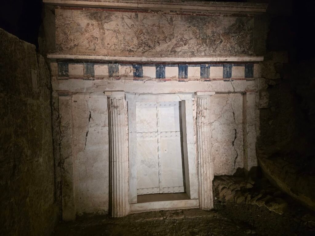 Façade of the Tomb of Philip II, designed as an ancient Greek temple with Doric half-columns, a marble door, and two friezes—including a Doric triglyph and metope frieze and an Ionic Hunt Frieze—symbolizing Macedonian royal power and identity. Museum of the Royal Tombs of Aigai, Expats Athens, Expats Greece, Xpat.gr