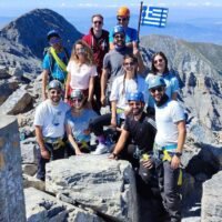 Group of hikers at the summit area of Mount Olympus with the Greek flag during an Unlimited Adrenaline mountain adventure featured on Xpat.gr.