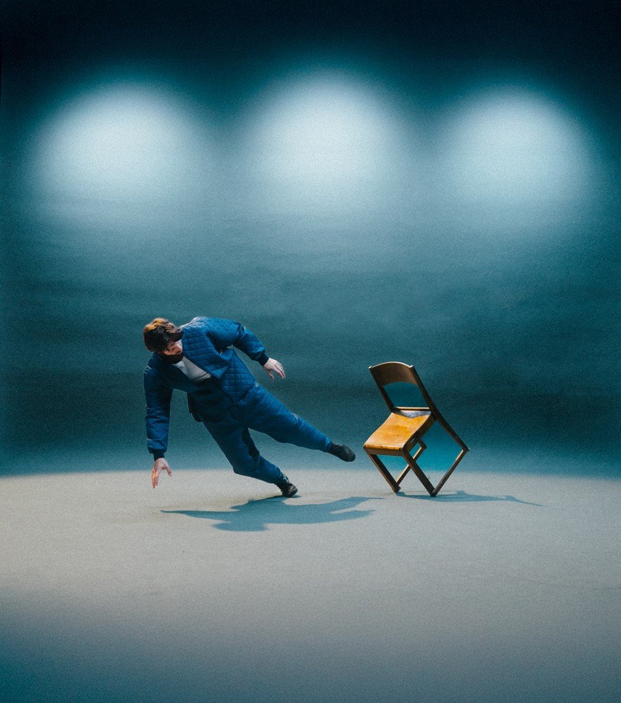 Performer on stage beside a chair in Tempo by Kalle Nio and Fernando Melo.