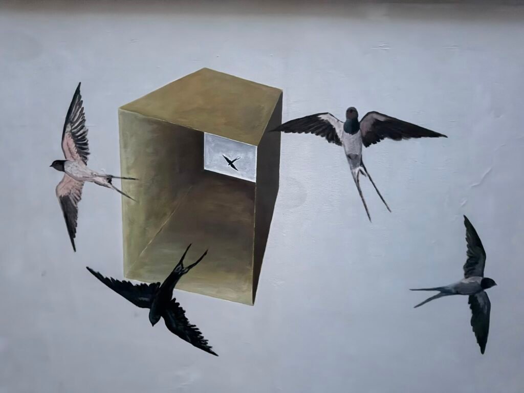 A street mural in Kalamata depicting swallows flying around a three-dimensional box,