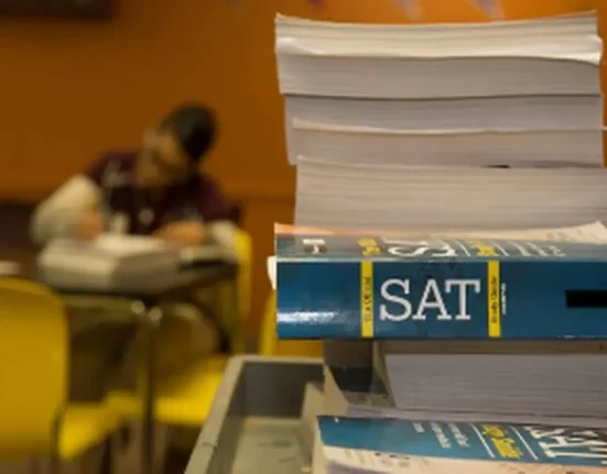 SAT preparation books in the foreground as a student studies in a classroom