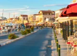 Aegina Town waterfront with moored boats, seafront buildings and outdoor cafés.