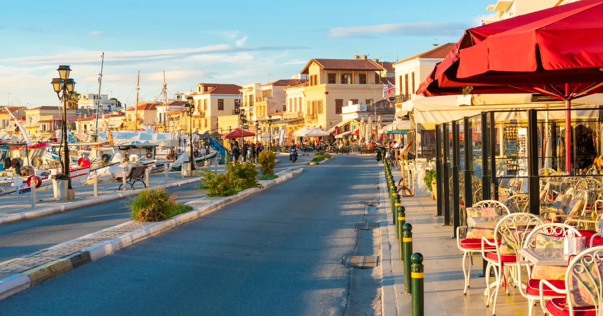 Aegina Town waterfront with moored boats, seafront buildings and outdoor cafés.
