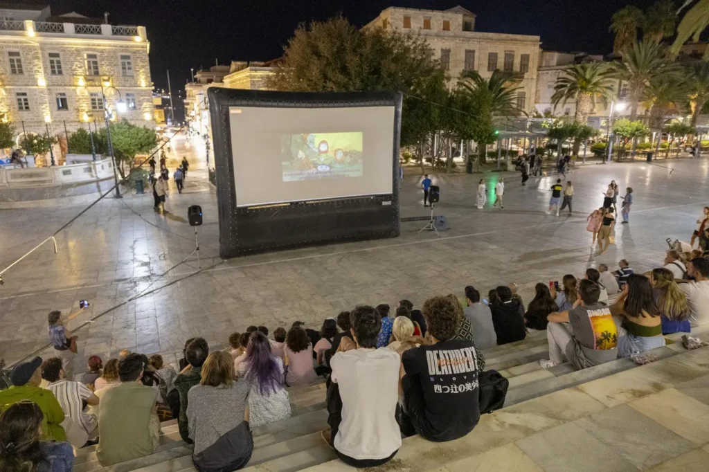 Crowds watching an outdoor ANIMASYROS film screening in a square in Hermoupolis