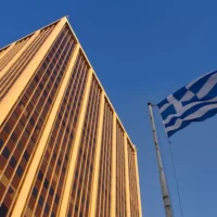 Athens Tower and the Greek flag against a clear blue sky