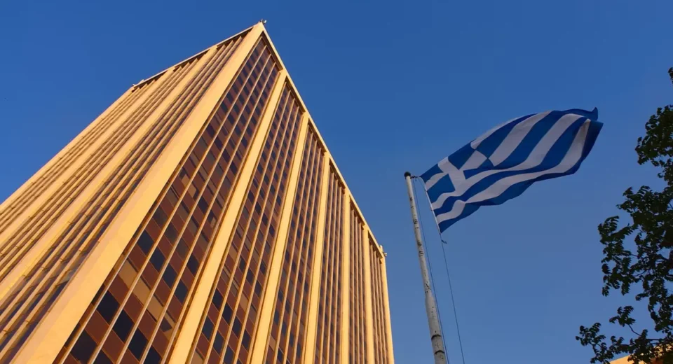 Athens Tower and the Greek flag against a clear blue sky