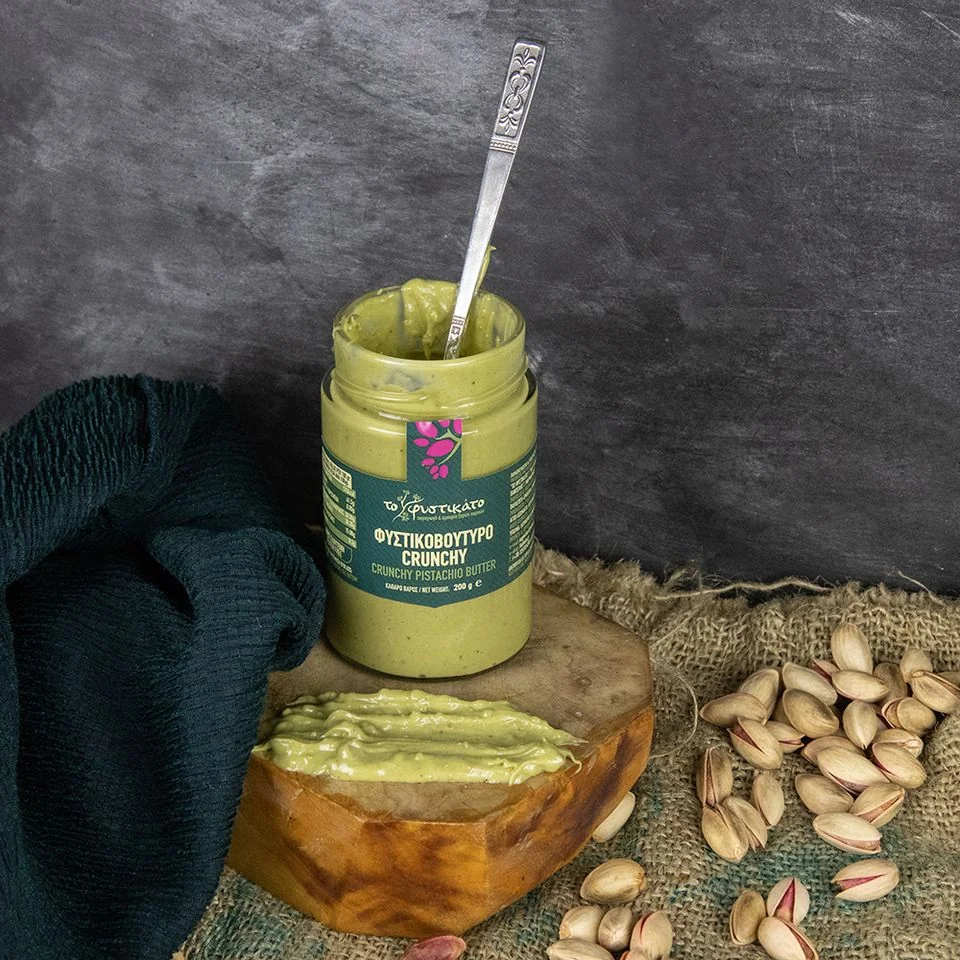 Open jar of Fistikato crunchy pistachio butter beside bread and pistachios.
