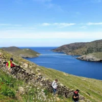 Hikers walking along a hillside trail above the Aegean Sea on Kythnos island, Greece.