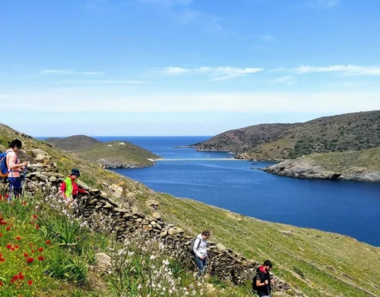 Hikers walking along a hillside trail above the Aegean Sea on Kythnos island, Greece.