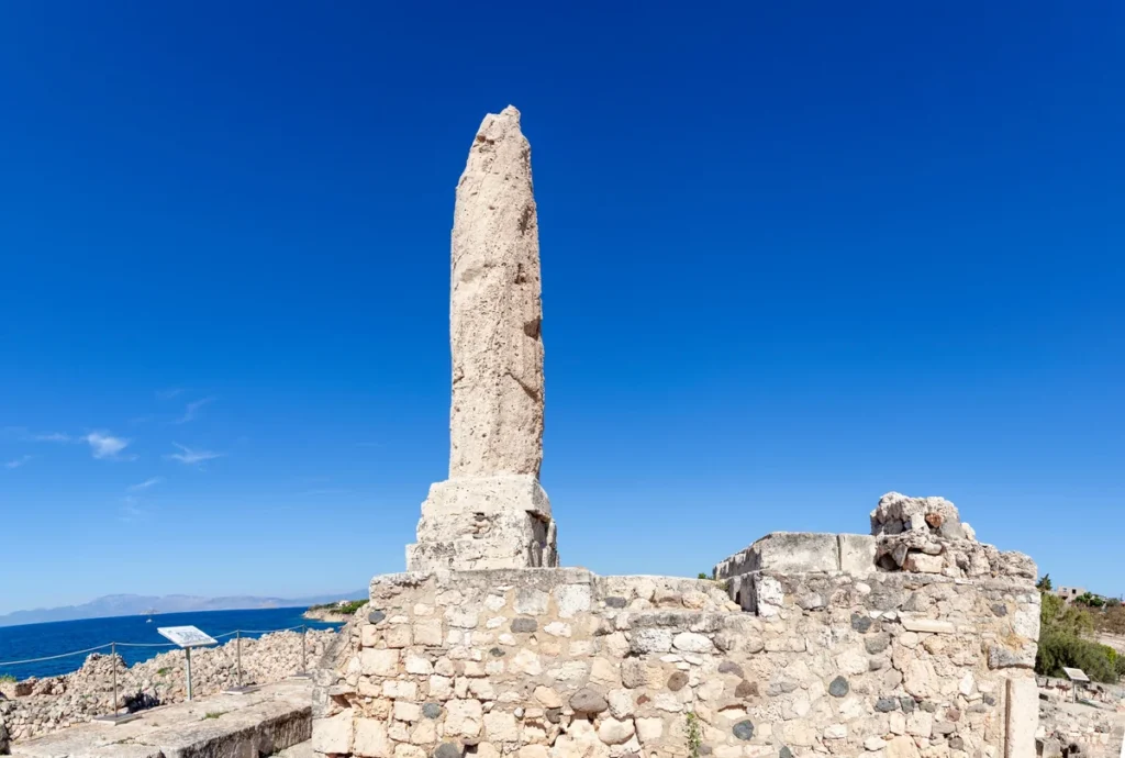 The surviving column of the Temple of Apollo above stone ruins at Kolona, with the sea behind.