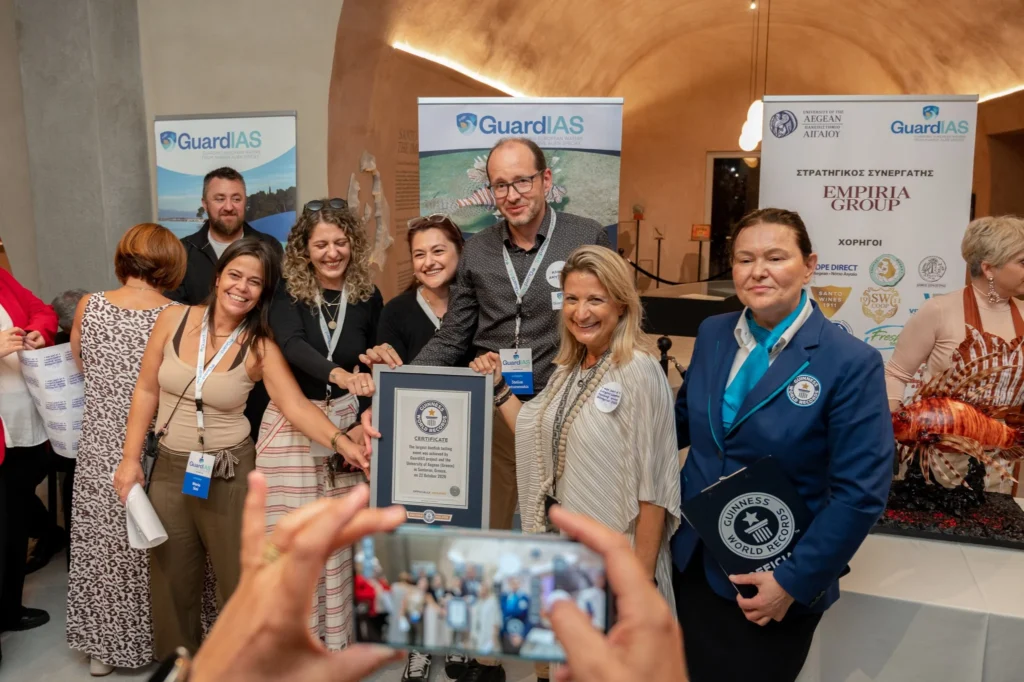 GuardIAS project representatives with a Guinness World Records adjudicator displaying the official certificate for the largest lionfish tasting event in Santorini.