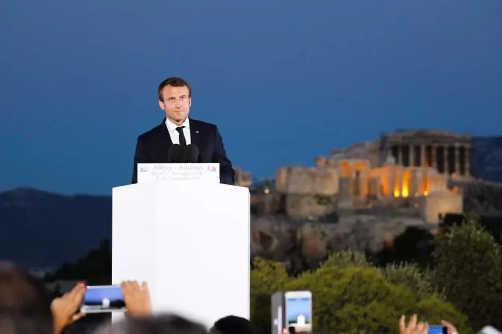 French President Emmanuel Macron speaking at the Pnyx with the Acropolis illuminated behind him